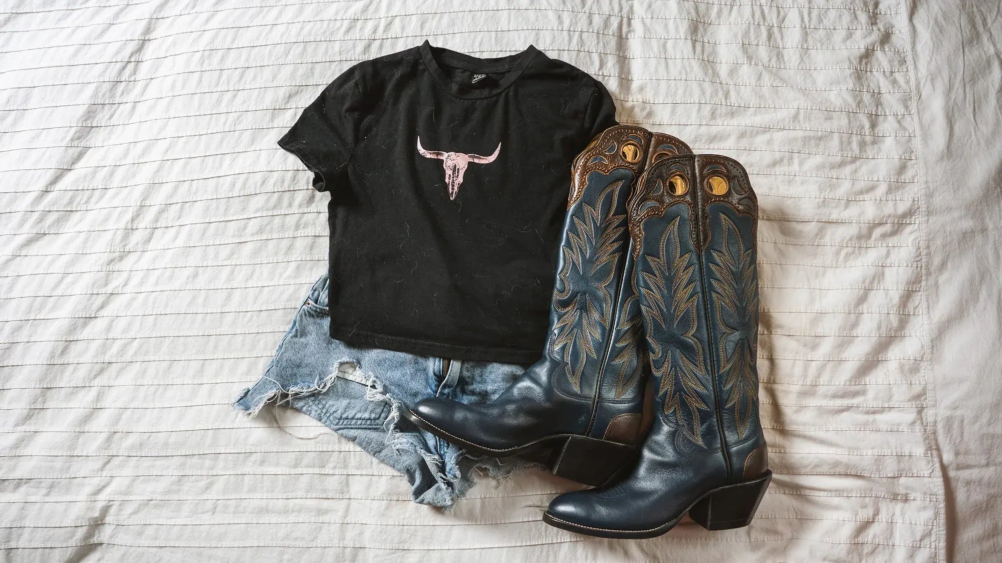 A pair of black cowboy boots laid out with a Paul Bond tee