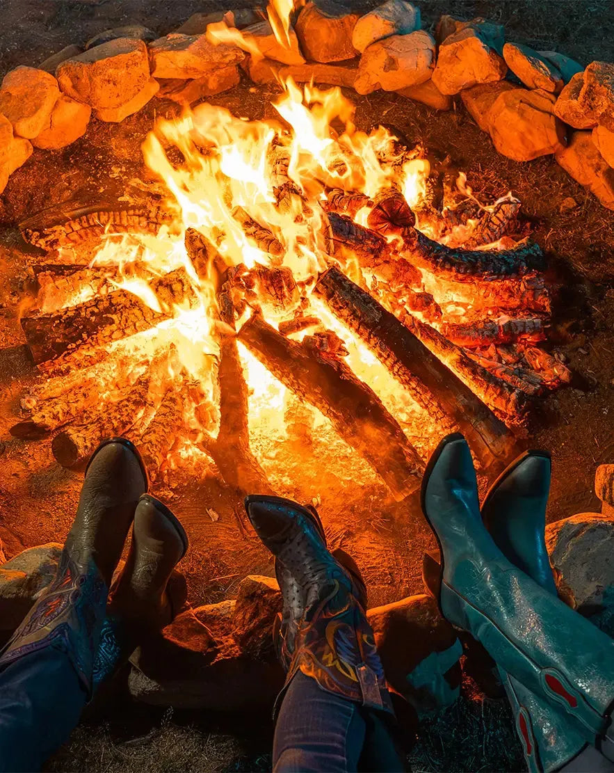 Friends in cowboy boots with their feet up around a campfire