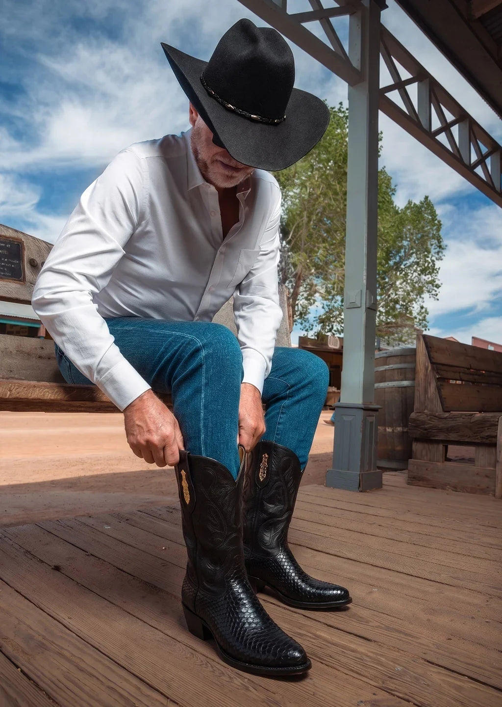 A man pulling on black python Paul Bond boots on a wooden boardwalk